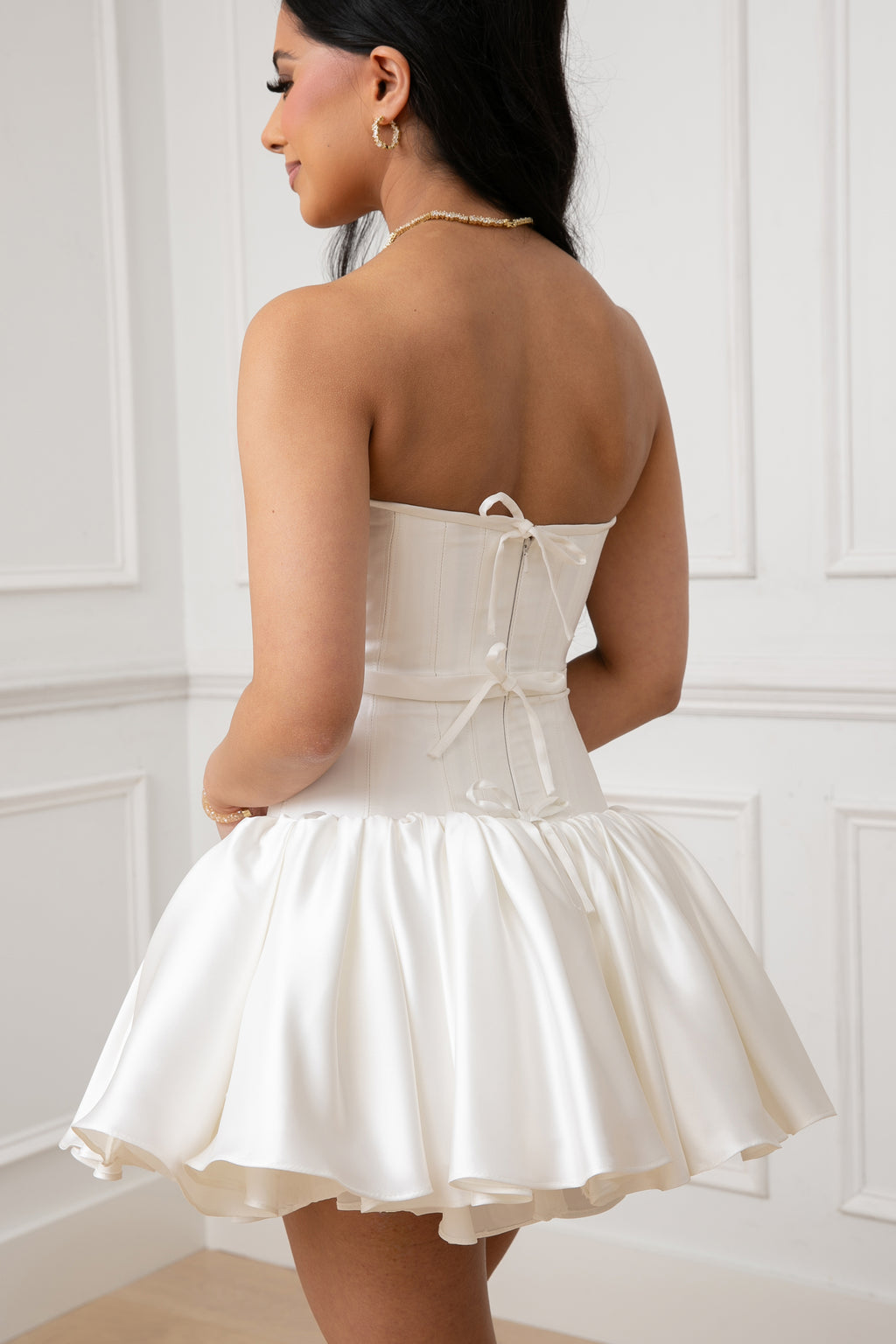 The Duchess Dress by Brunell by Shar, close-up of the back white satin mini dress, featuring delicate bow accents, dainty belt, an invisible zipper, and a gathered drop-waist skirt.