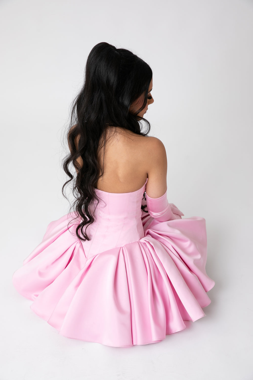Back view of The Palais Dress by Brunell by Shar, luxury pink strapless satin corset mini dress with layered pleated skirt and matching opera gloves.